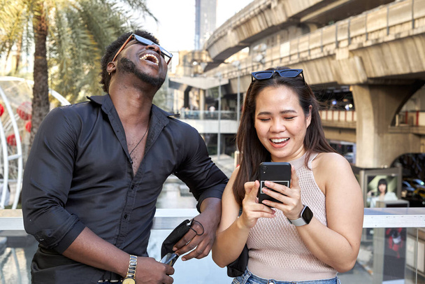 Amis multiraciaux riant et utilisant le mobile à côté d'un centre commercial - Photo, image