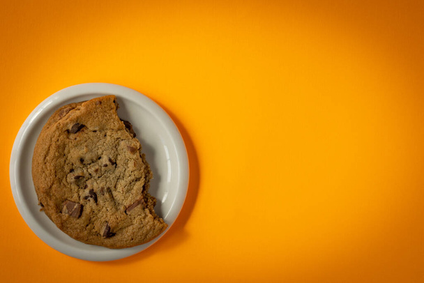 Broken chocolate chip cookie on a saucer surrounded by circular gradient from orange to yellow background - Foto, immagini
