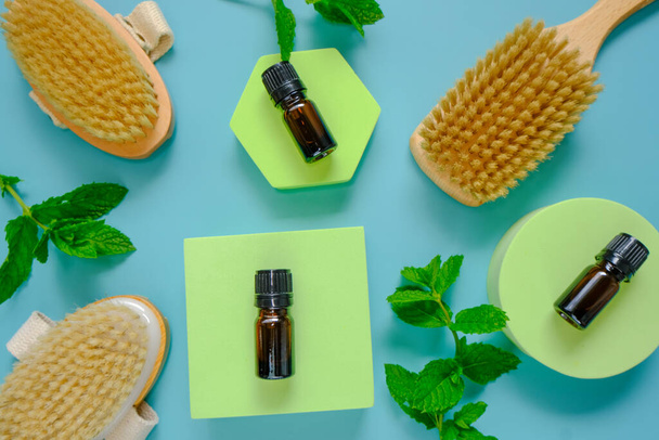 Peppermint essential oil.glass bottle and body brushes with natural bristles on green podiums against a blue background .Natural Organic Peppermint Oil  - Photo, Image