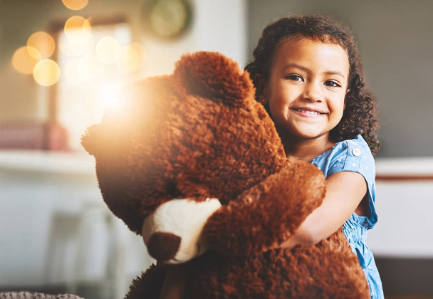 I dont go anywhere without him. Portrait of a little girl holding her teddy bear at home. - Photo, Image