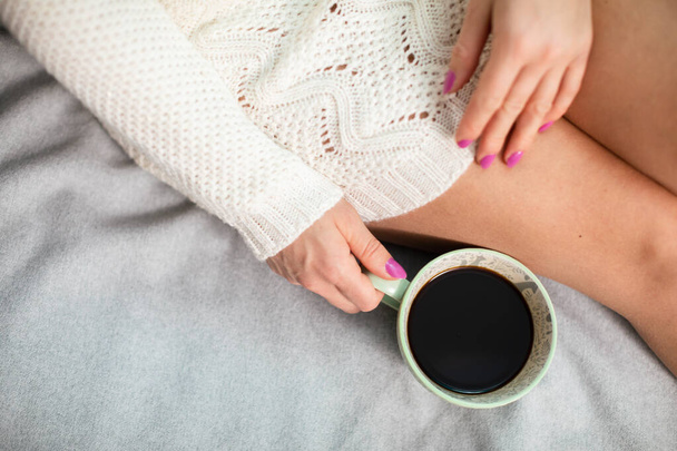 Woman sits on bed with cup of coffee. Neat legs. - Fotografie, Obrázek