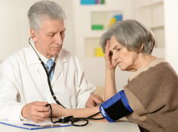 Médico de edad avanzada que mide la presión arterial
 - Foto, imagen