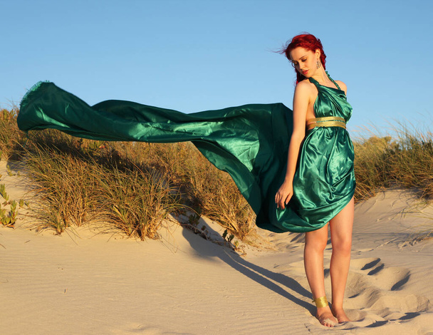 Täyspitkä muotokuva punatukkainen nainen yllään revitty haaksirikkoutunut vaatteita. Seisova poseeraa eleet käsissä Rocky Ocean Beach maisema tausta. - Valokuva, kuva