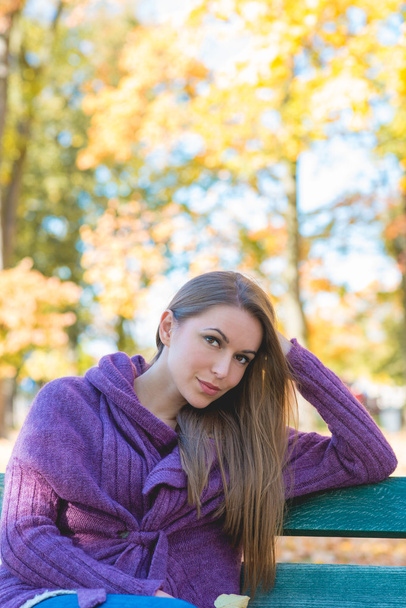 Όμορφη γυναίκα σε φθινόπωρο στολή κάθεται σε παγκάκι - Φωτογραφία, εικόνα