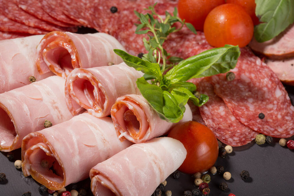 meat assortment of sausage, bacon, prosciutto decorated with basil leaves, close-up - Fotografie, Obrázek