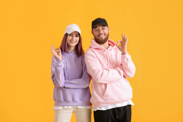 Cool jeune couple à capuche montrant OK sur fond de couleur - Photo, image