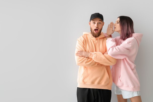 Gossiping young couple in hoodies on light background - Foto, Imagem