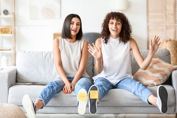 Happy sisters with sticky notes on shoes sitting in living room - Photo, Image