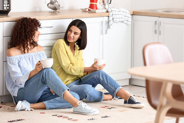 Beautiful sisters sitting on floor and drinking tea in kitchen - Photo, Image
