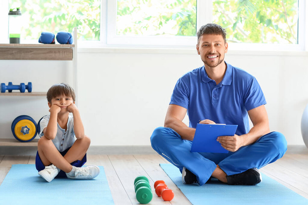 Male trainer with clipboard and little boy in gym - Фото, зображення