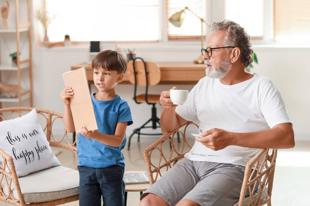 Маленький хлопчик з журналом і його дід п'є чай вдома
 - Фото, зображення