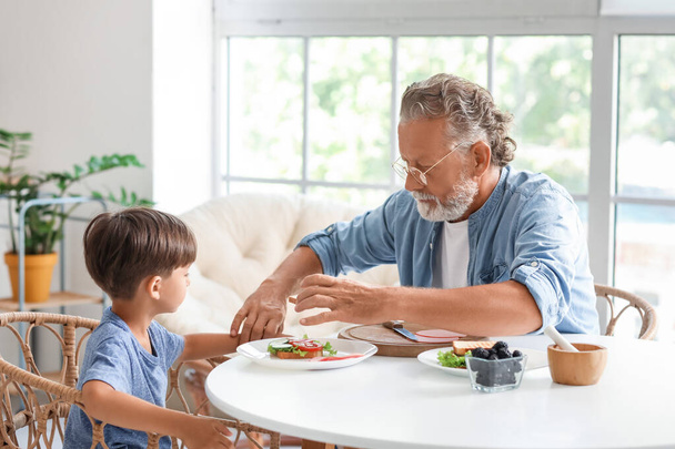 Kleine jongen ontbijten met zijn grootvader aan tafel in de keuken - Foto, afbeelding