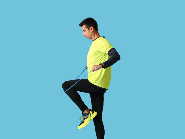 Sporty young man with jumping rope on color background - Foto, Bild