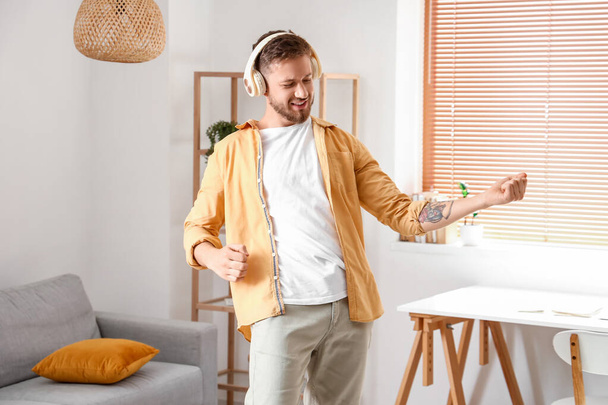 Young man in headphones playing imaginary guitar at home - Фото, зображення
