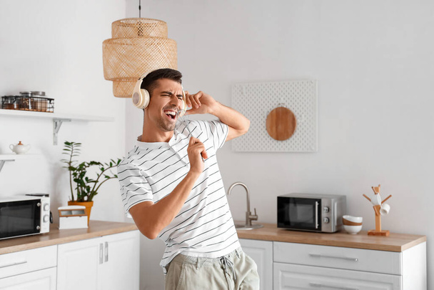 Young man with headphones singing in kitchen - Foto, imagen