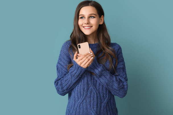 Mooie jonge vrouw met mobiele telefoon op blauwe achtergrond - Foto, afbeelding