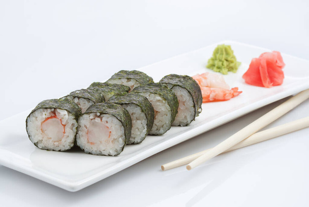 sushi vagy tekercs hosszú tányéron, fa pálcika, vörös gyömbér és wasabi, fehér alapon - Fotó, kép