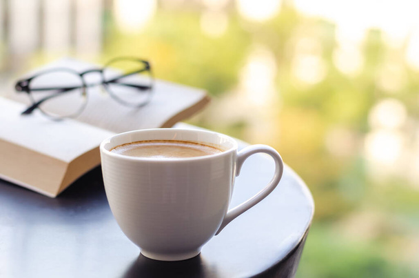 Selektivní zaměření bílé šálku kávy klade na stůl na balkóně s knihou a brýlemi. Relaxační doma koncept. - Fotografie, Obrázek