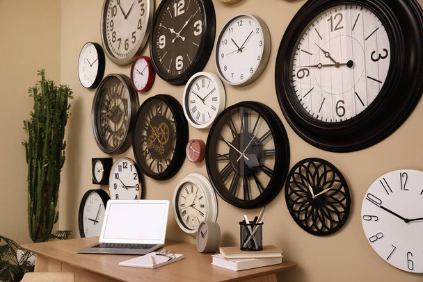 Stylish room interior with collection of wall clocks and workplace - Foto, afbeelding