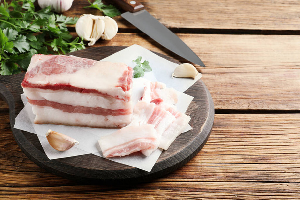 Tasty salt pork with garlic and parsley on wooden table, space for text - Фото, изображение