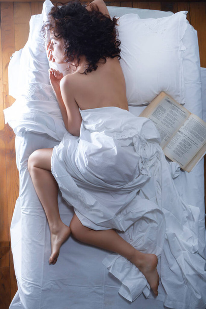 Fotózás egy egynapos nőről, aki egy ágyban alszik, fehér lepedővel és nyitott könyvvel.  - Fotó, kép