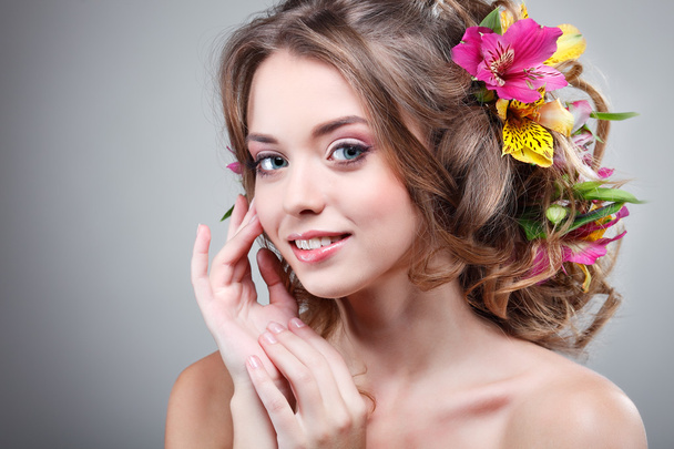 Beautiful  girl, isolated on a light - grey  background with varicoloured flowers  in hairs, emotions, cosmetics - Foto, afbeelding