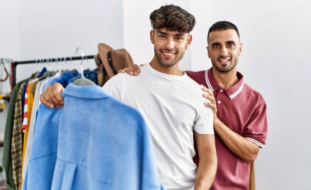 Молода пара іспаномовних посміхається щасливий тримає сорочку в магазині одягу
. - Фото, зображення