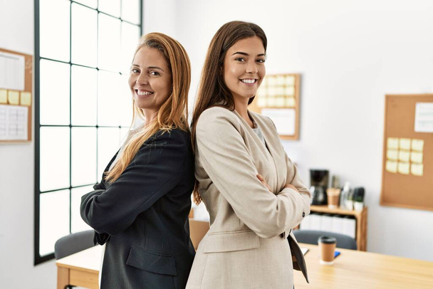 Работники бизнеса матери и дочери улыбаются уверенно стоя со скрещенными руками в офисе - Фото, изображение