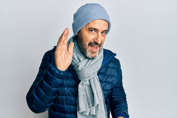 Middle age hispanic man wearing winter style smiling with hand over ear listening and hearing to rumor or gossip. deafness concept.  - Photo, Image