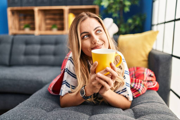 Jovem loira bebendo café deitado no sofá em casa - Foto, Imagem