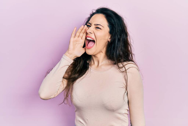 若いヒスパニック系の女性は、カジュアルな服を叫び、口の中で手で横に大声で叫んで身に着けている。コミュニケーションの概念.  - 写真・画像