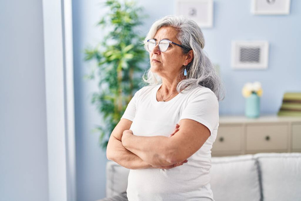 Donna di mezza età con espressione seria in piedi con le braccia incrociate gesto a casa - Foto, immagini