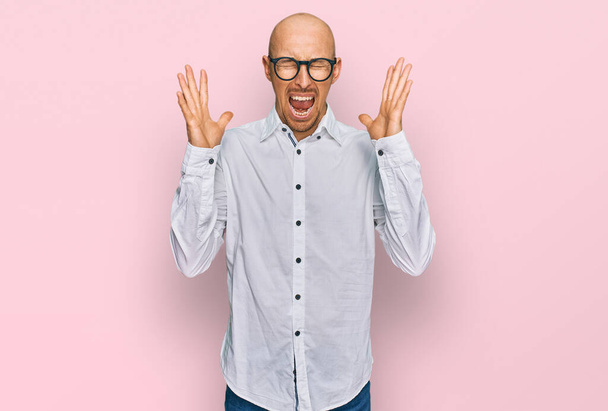 Bald man with beard wearing business shirt and glasses celebrating mad and crazy for success with arms raised and closed eyes screaming excited. winner concept  - Valokuva, kuva
