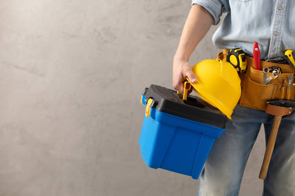 Worker man holding construction helmet tool and toolbox near concrete or cement wall. Male hand and hard hat for house room renovation. Home renovation concept - Φωτογραφία, εικόνα