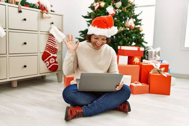 Middle age hispanic woman having video call sitting by christmas tree at home. - Fotoğraf, Görsel
