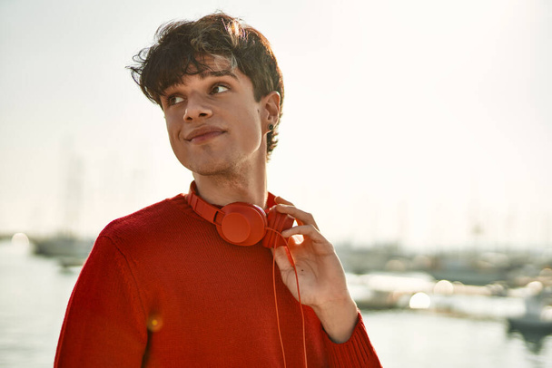Joven hombre hispano sonriendo feliz usando auriculares en la playa - Foto, Imagen