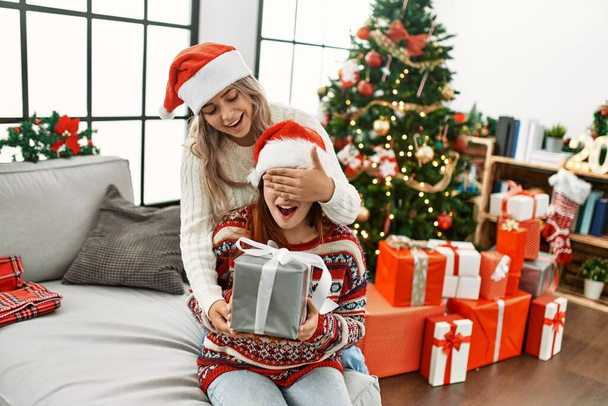 Woman couple surprise with gift sitting by christmas tree at home - Photo, Image
