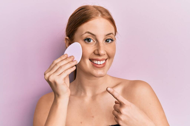 Young irish woman holding makeup sponge smiling happy pointing with hand and finger  - Fotografie, Obrázek