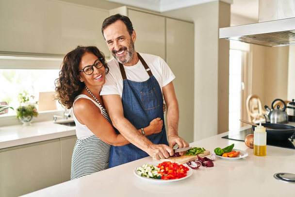 Middle age hispanic couple smiling confident and hugging each other cooking at kitchen - Photo, Image