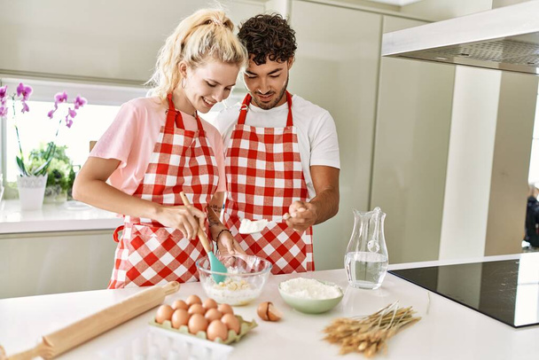Молода пара посміхається щасливим змішуванням інгредієнтів, щоб зробити тісто для домашнього хліба на кухні
. - Фото, зображення