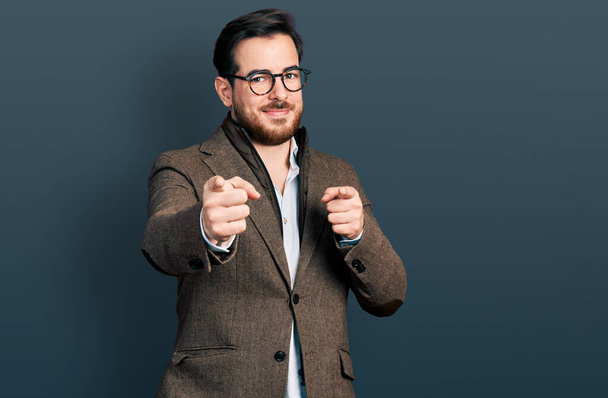 Homem hispânico jovem vestindo jaqueta de negócios e óculos apontando os dedos para a câmera com rosto feliz e engraçado. boa energia e vibrações.  - Foto, Imagem