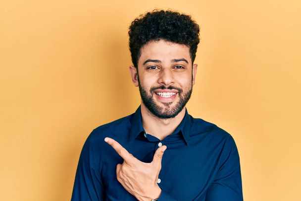 Young arab man with beard wearing casual shirt cheerful with a smile of face pointing with hand and finger up to the side with happy and natural expression on face  - Foto, immagini