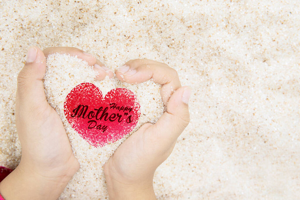 Close up of little girl hands holding sand with happy mothers day text on the heart symbol - 写真・画像