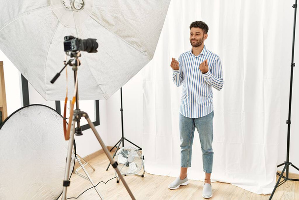 Arabischer junger Mann posiert als Model im Fotostudio und macht Geld-Geste mit den Händen, verlangt Gehaltszahlung, Millionärsgeschäft  - Foto, Bild