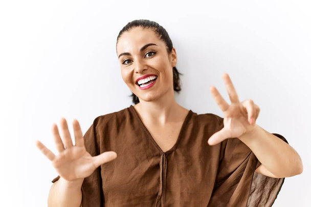Mladá brunetka žena stojící nad izolovaným pozadím ukazující a ukazující nahoru s prsty číslo osm a usmívající se sebevědomě a šťastně.  - Fotografie, Obrázek