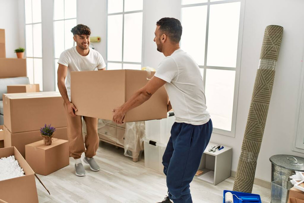 Two hispanic men couple smiling confident holding cardboard box at new home - Fotoğraf, Görsel