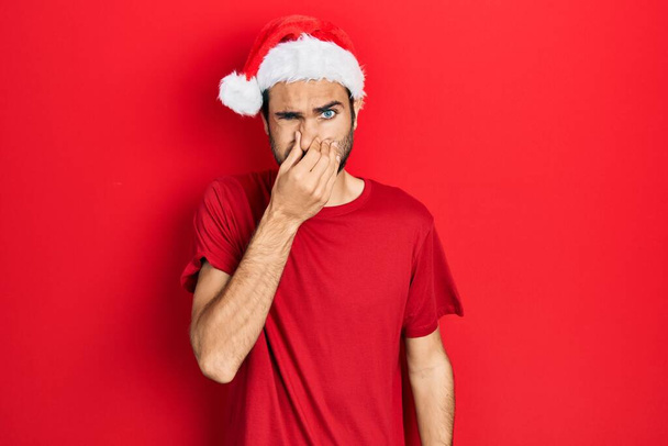 Młody Hiszpan w świątecznym kapeluszu pachnie czymś śmierdzącym i obrzydliwym, nie do zniesienia, wstrzymując oddech palcami na nosie. nieprzyjemny zapach  - Zdjęcie, obraz