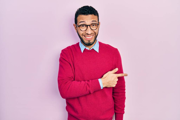 Hombre hispano con barba vistiendo camisa de negocios y gafas apuntando a un lado preocupado y nervioso con el dedo índice, preocupado y sorprendido expresión  - Foto, imagen