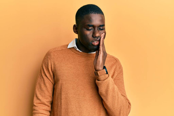 Νεαρός Αφροαμερικάνος που φοράει καθημερινά ρούχα αγγίζοντας το στόμα με το χέρι με επώδυνη έκφραση λόγω πονόδοντος ή οδοντικής πάθησης στα δόντια. οδοντίατρος  - Φωτογραφία, εικόνα