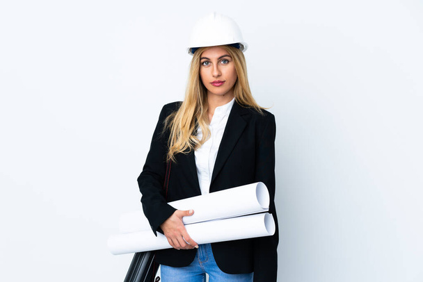 Młoda architekt kobieta w kasku i trzymając plany na odizolowanym białym tle trzyma ręce skrzyżowane - Zdjęcie, obraz